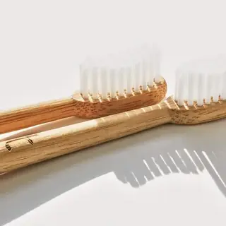 Two bamboo toothbrushes with white bristles on a light background.