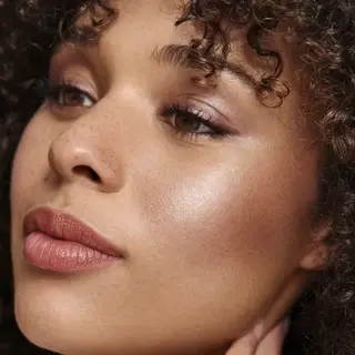 Close-up of a person with curly hair and glowing skin, looking to the side.