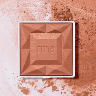 Square bronzer compact with "rms" embossed, surrounded by loose powder.