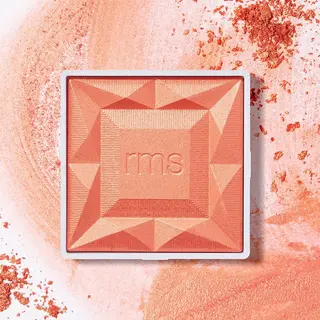 Coral blush compact with "rms" embossed, surrounded by scattered powder.