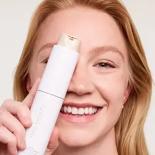Smiling person holding rms beauty foundation bottle.