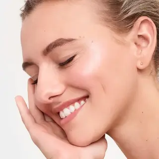 Woman with closed eyes smiling, touching her cheek.