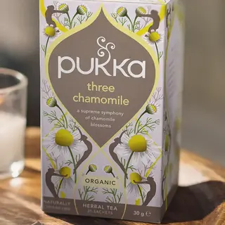 Pukka Three Chamomile tea box on wooden tray, 20 sachets, organic herbal blend.