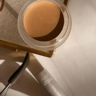 Open jar of beige cream on a table with a tube and tool nearby.