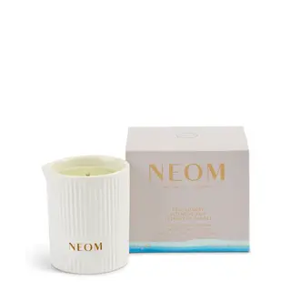 White NEOM candle with ribbed texture next to its box. Text: "Real Luxury Intensive Skin Treatment Candle".