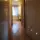 Hallway with wooden floor, open door, and a lit room with a chair and plant visible at the end.