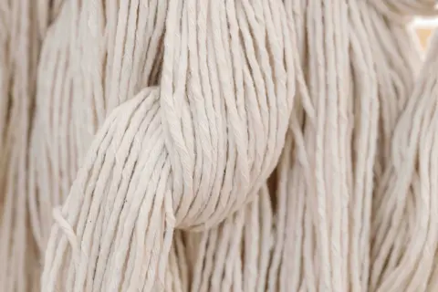 Close-up of cream-coloured yarn strands hanging vertically.