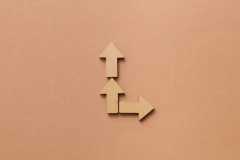 Three cardboard arrows on a brown background, pointing up and right.