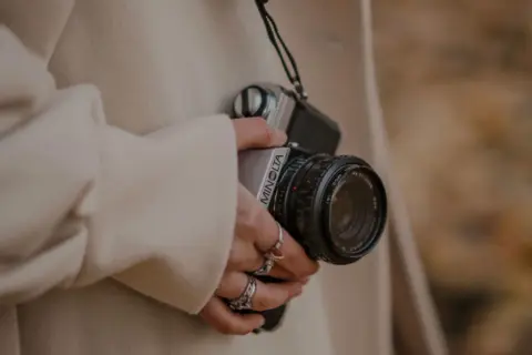 Person in beige coat holding a vintage Minolta camera.