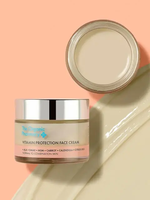 Vitamin Protection Face Cream jar and open lid on peach background. Cream spread nearby.