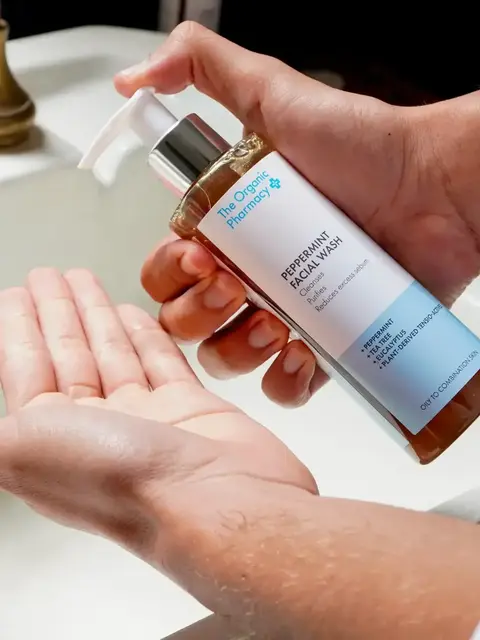 Person dispensing peppermint facial wash into hand by a sink.