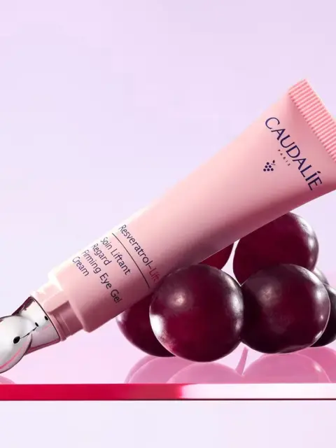 Pink tube of Caudalie Resveratrol Lift Eye Gel on red grapes.