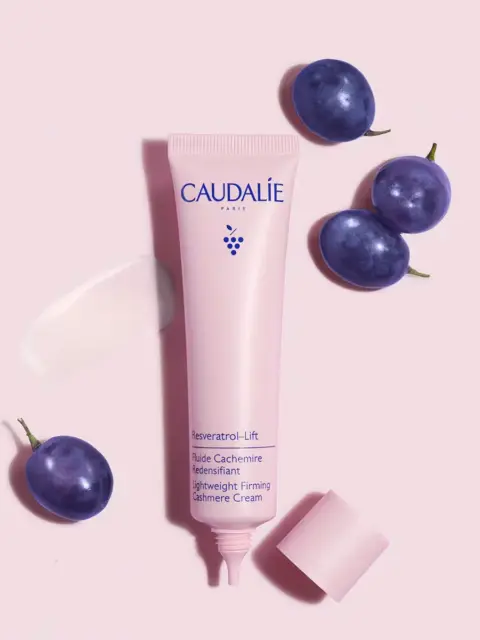 Pink tube of Caudalie cream with grapes on a pink background.