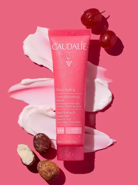 Caudalie VinoHydra cream tube on pink background with grapes and shea nuts.