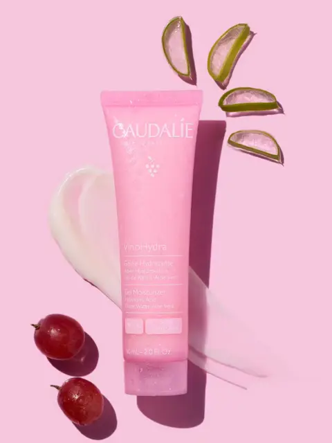 Pink Caudalie VinoHydra gel moisturiser with aloe slices and grapes on pink background.