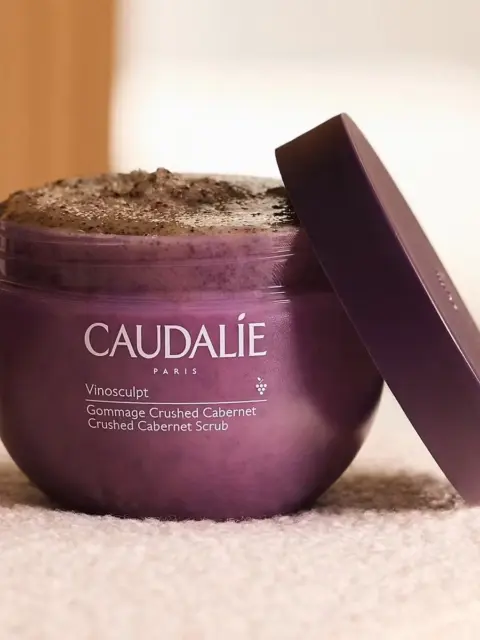 Caudalie Vinosculpt Crushed Cabernet Scrub in a purple jar with lid ajar.