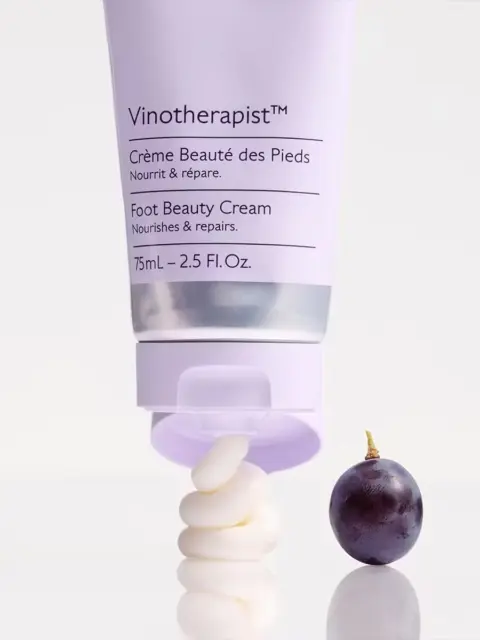 Vinotherapist Foot Beauty Cream tube with cream swirl and a grape on a white surface.
