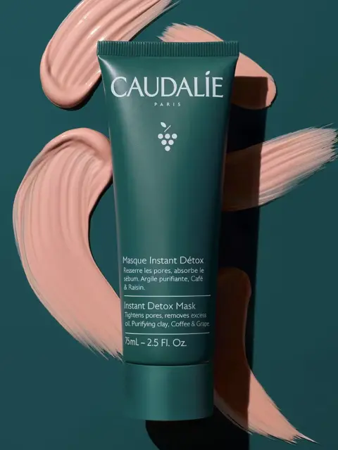 Green tube of Caudalie Instant Detox Mask on dark background with pink cream swirls.