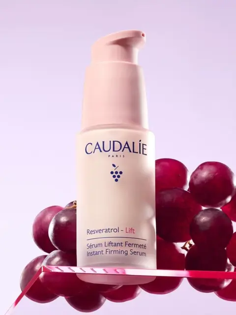 Caudalie Resveratrol Lift serum bottle with grapes on a pink background.