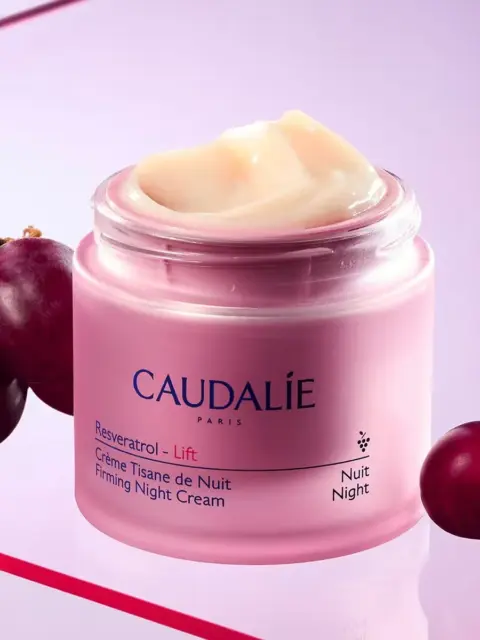 Caudalie Resveratrol Lift Firming Night Cream jar with grapes on a pink background.