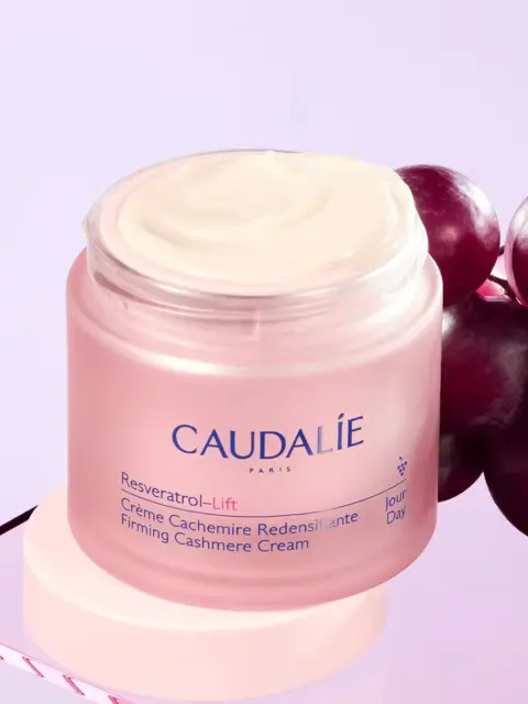 Caudalie Resveratrol-Lift Firming Cashmere Cream jar with grapes on a purple background.