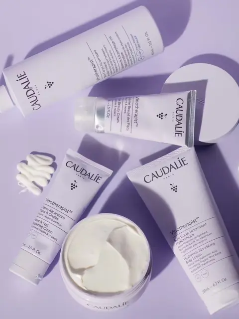 Caudalie skincare products on a purple surface, including creams and lotions.