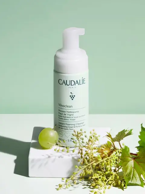 Caudalie Vinoclean foaming cleanser with grape and vine leaves on a white surface.