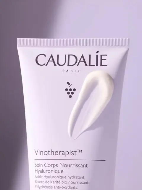 Caudalie Vinotherapist body cream tube with cream smear on a purple background.