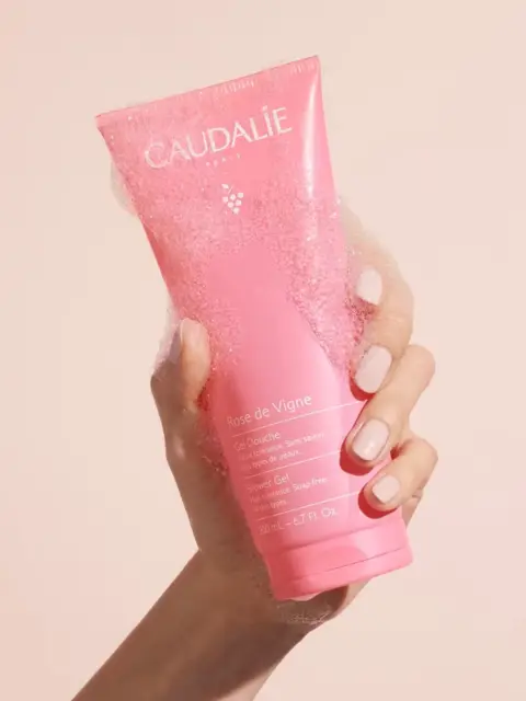 Hand holding pink Caudalie Rose de Vigne shower gel with bubbles.