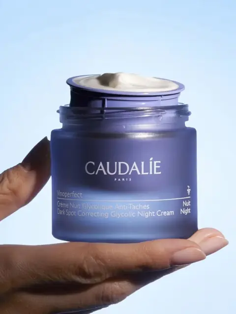 Caudalie Vinoperfect Night Cream jar held against a blue background.