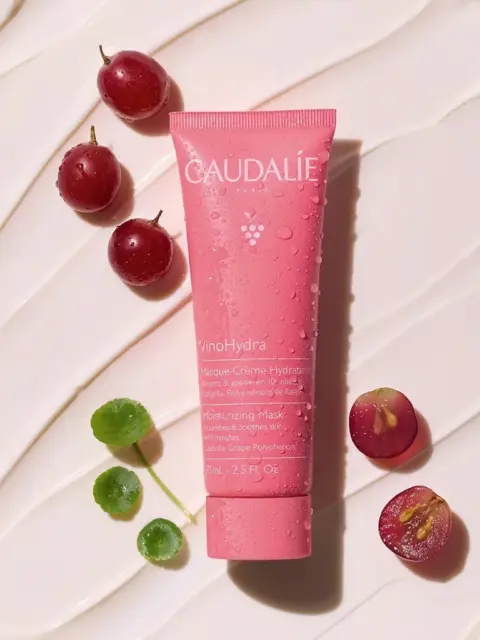 Pink Caudalie VinoHydra mask tube with grapes and leaves on a creamy background.