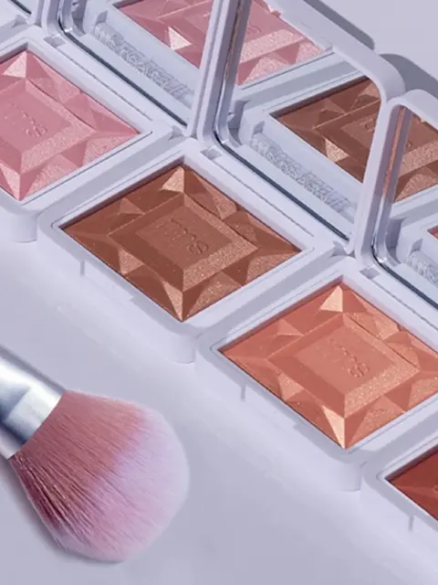 Makeup compacts with mirrors and a pink brush on a white surface.