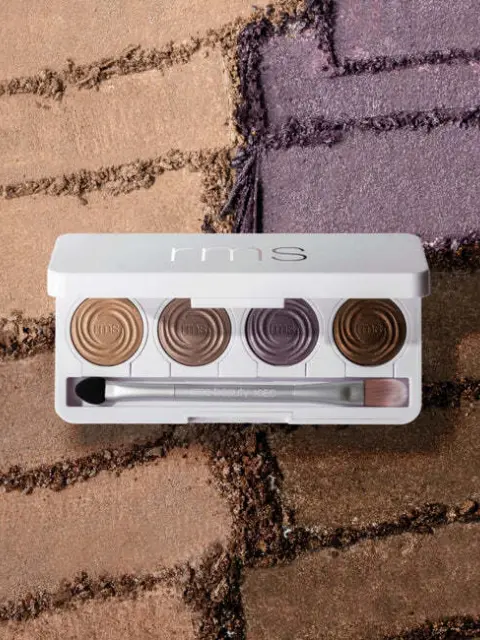 RMS eyeshadow palette with five shades and brush on textured background.