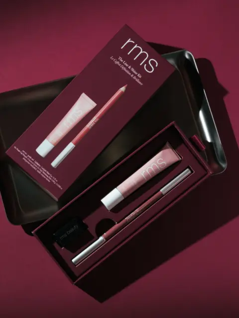 RMS lip kit with gloss, pencil, and sharpener in a dark red box on a matching background.
