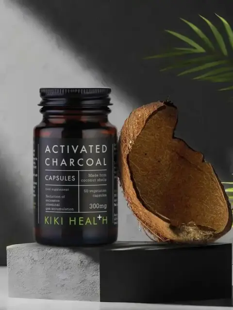 Activated charcoal capsules bottle beside a coconut shell on a grey surface.