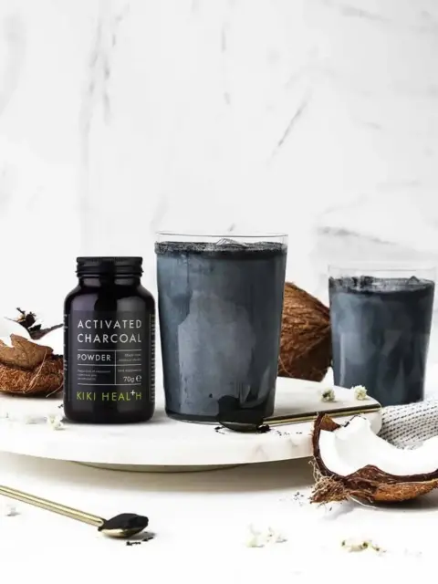 Activated charcoal powder with coconut and two charcoal drinks on a marble surface.