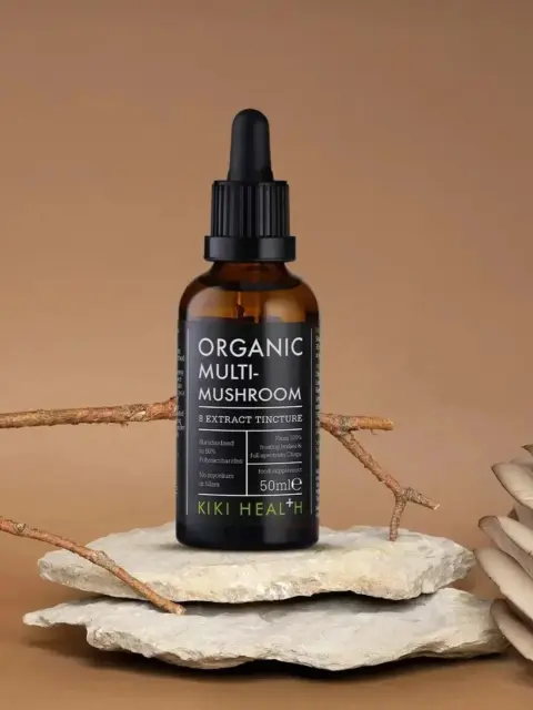 Organic Multi-Mushroom tincture bottle on stone with branches and mushrooms.