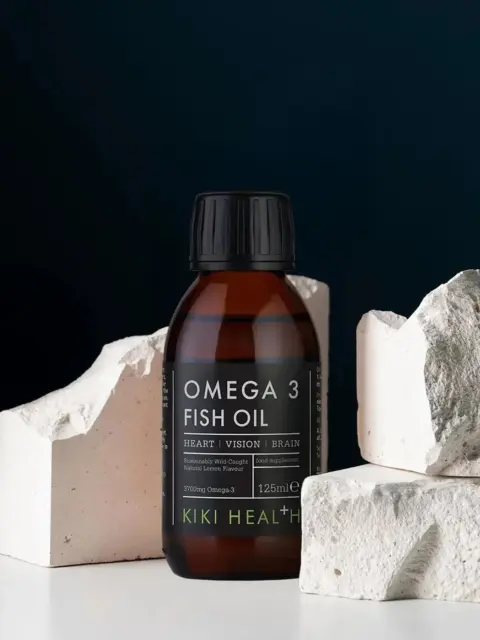 Omega 3 Fish Oil bottle with white rocks, dark background.