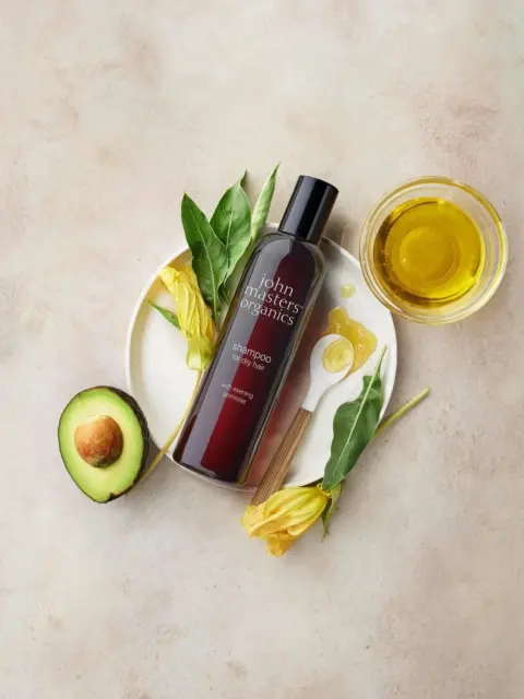 Shampoo bottle with avocado, leaves, yellow flowers, honey, and oil on a plate.