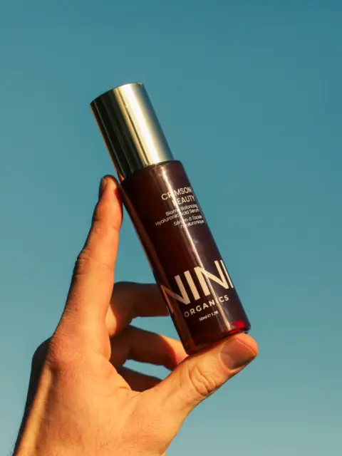 Hand holding NINI Organics bottle against clear blue sky.