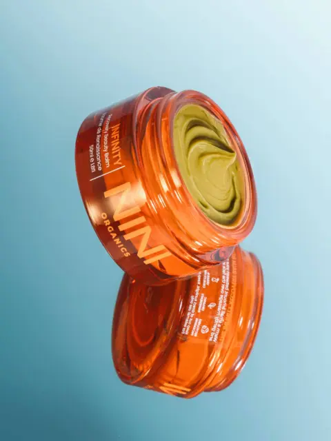 Orange jar of green skincare cream on a reflective surface.