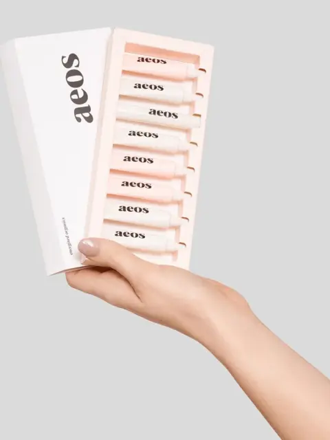 Hand holding aeos skincare set with six tubes in a white box.