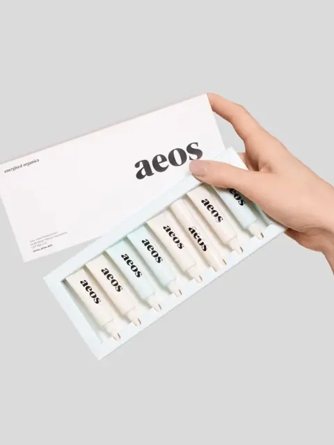 Hand holding aeos skincare set with six tubes in a box.