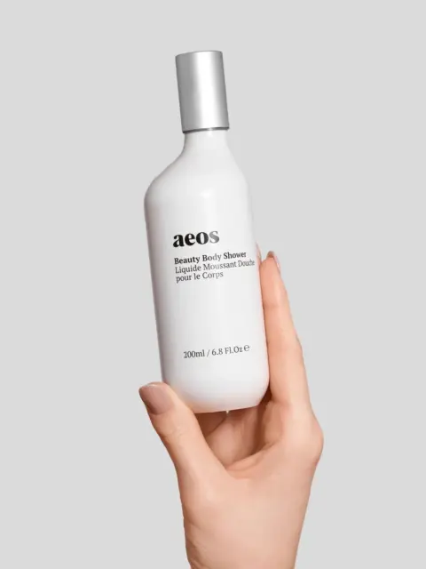 Hand holding aeos Beauty Body Shower bottle, 200ml, on grey background.