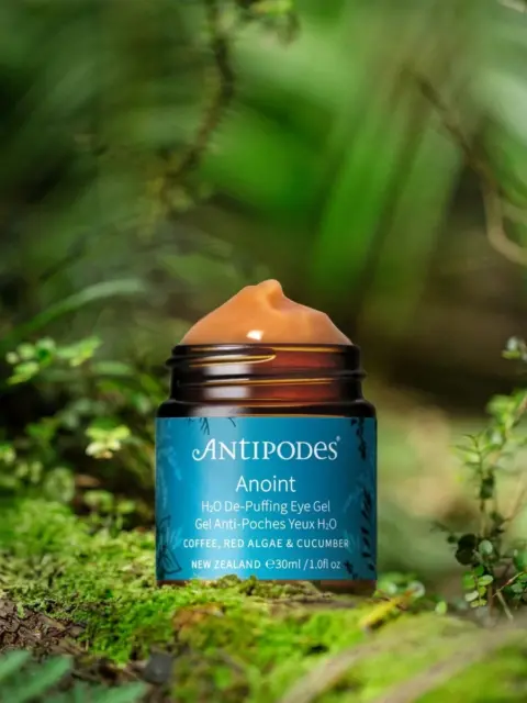 Antipodes Anoint Eye Gel jar on a forest floor with green foliage.