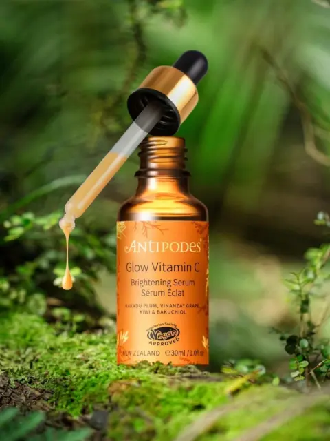 Antipodes Glow Vitamin C serum bottle with dropper in a lush green setting.