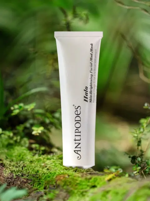 Antipodes Halo Skin-Brightening Facial Mud Mask tube on a mossy forest floor.
