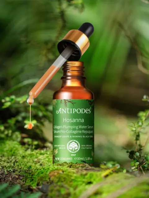 Antipodes Hosanna serum bottle with dropper, surrounded by lush green foliage.