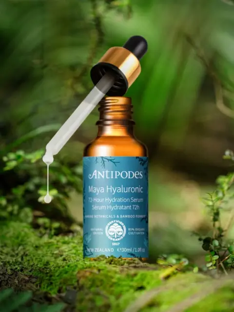 Brown bottle of Antipodes Maya Hyaluronic Serum with dropper in a lush green setting.