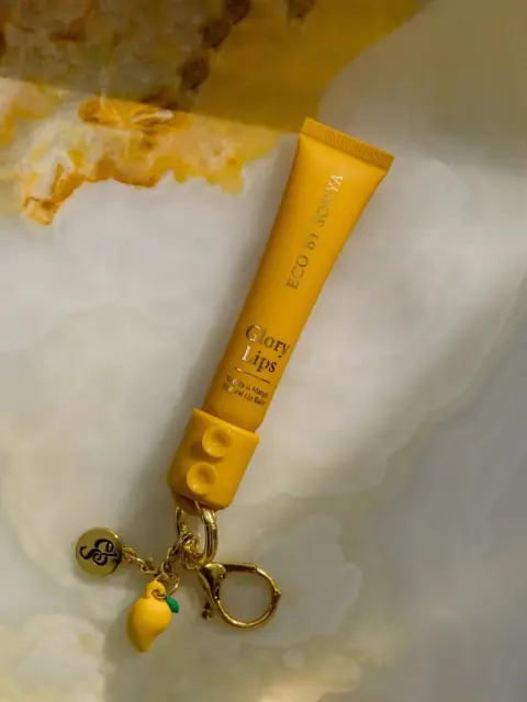 Yellow tube of Eco by Sonya Glory Lips balm with keychain on marble surface.